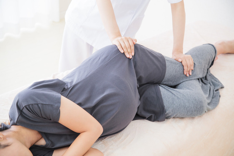 横向きになる妊婦と腰に右手をあてる白衣の人物